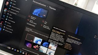Close-up of a laptop screen displaying the Windows Personalization Themes menu. Multiple theme options are visible, conveying a tech-focused feel.