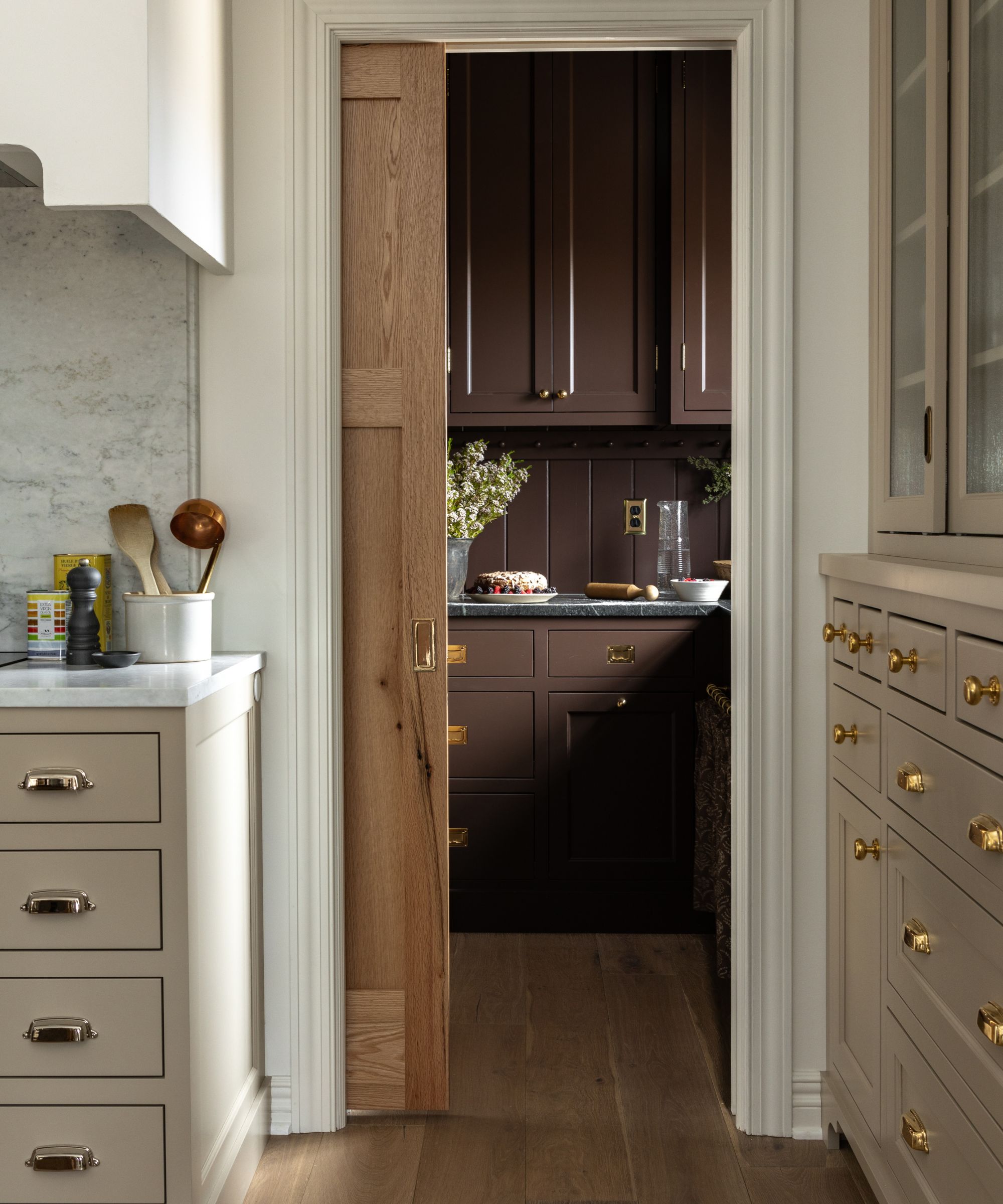 neutral warm beige farmhouse kitchen with a sliding door into a chocolate brown color drenched pantry