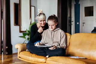 Mother and teen daughter sitting on the sofa at home looking at a tablet device together