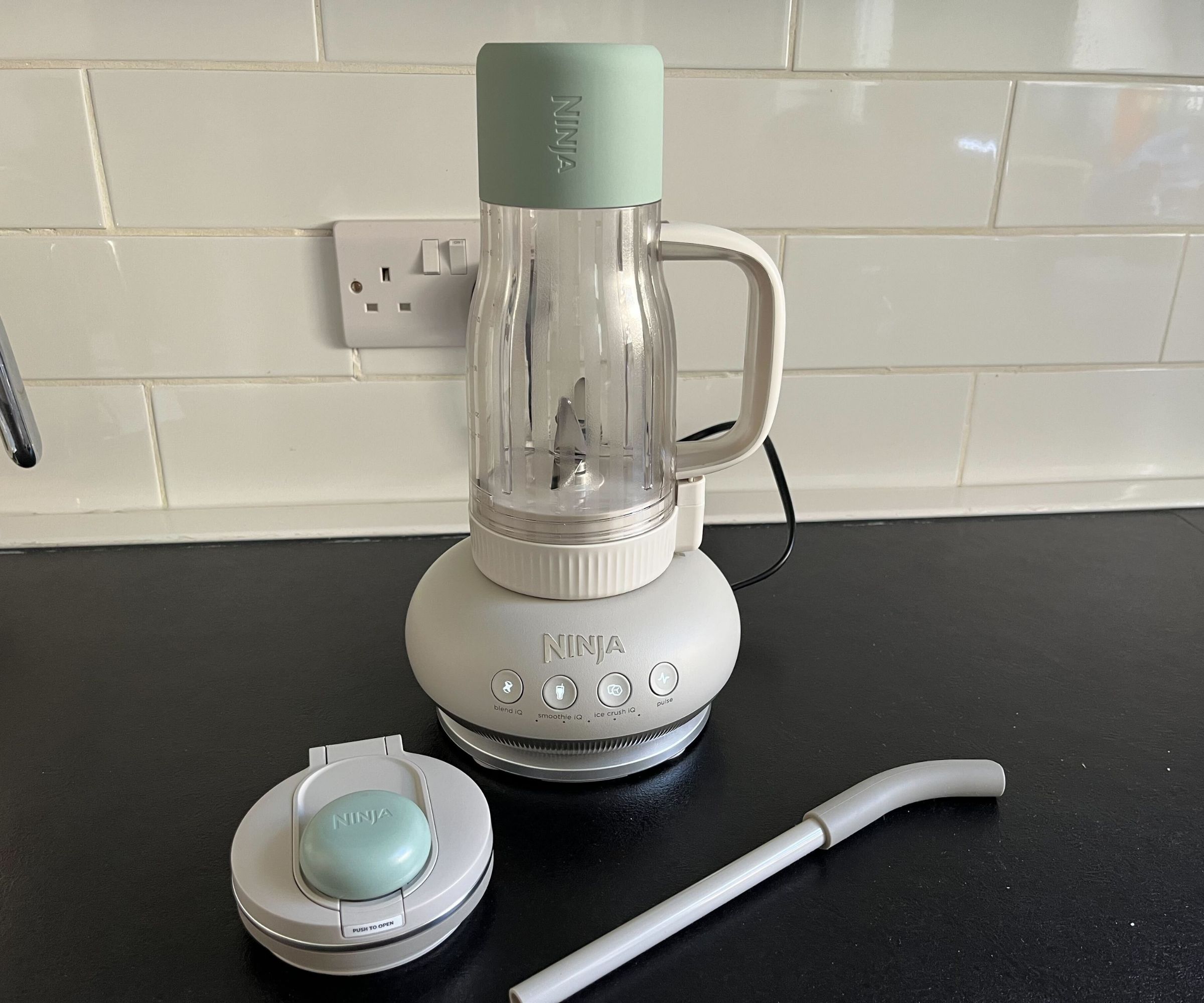 An upside down tumbler cup on a domed base forming a blender, with a lid and straw in front of it.