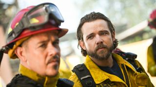 Bode Donovan (Max Thieriot) wearing firefighter gear and looking at another firefighter next to him.
