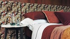 Patterned headboard and white bed with red, orange and mustard yellow throw blankets with red cushions