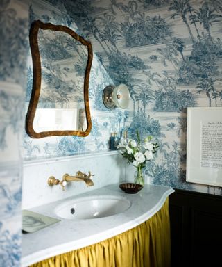 blue wallpapered bathroom in a traditional vintage print with an unexpected yellow sink skirt