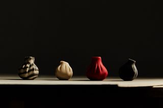 Four dumplings of different shades of black, cream, and red sit under dramatic lighting in a dark room.