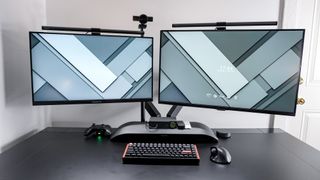 A dual-monitor desk setup with the SmallRig Camera Desk Mount holding up a webcam behind the displays