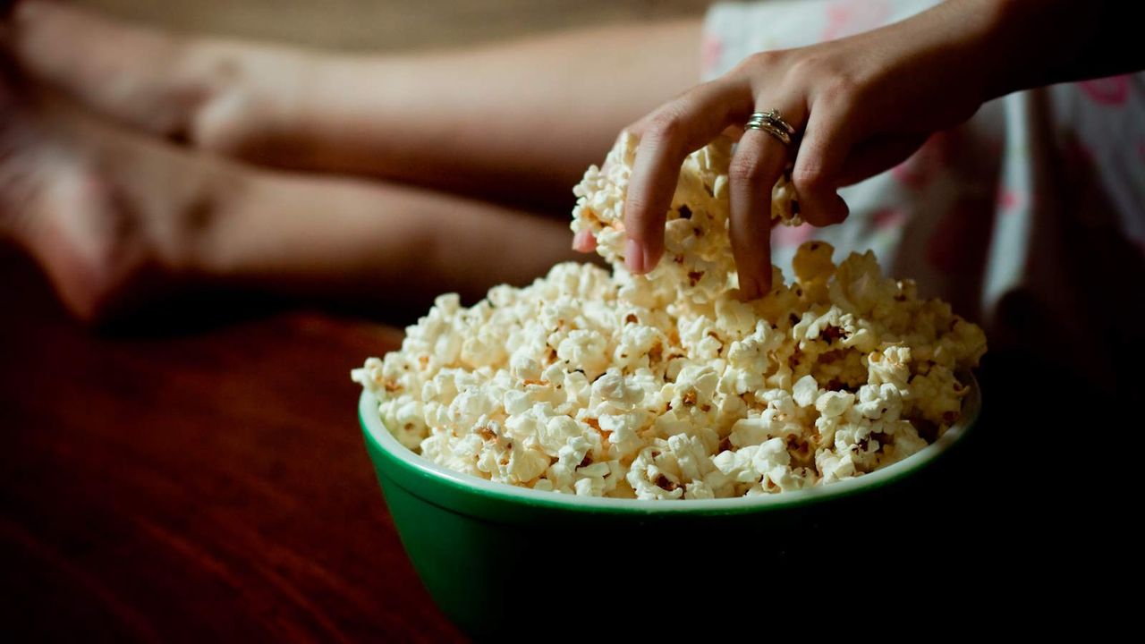 A hand grabbing popcorn from in a bowl