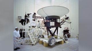 Engineers in white clothing carefully work on Voyager 2 spacecraft/