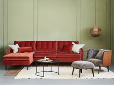 A rust coloured sofa with bold piping detail against a green wall