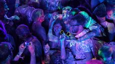 People at a party. There is a purple-tinted light and paint on the people is glowing under the UV light.