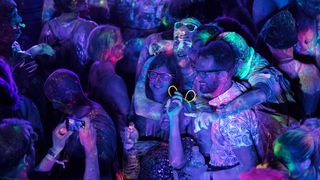 People at a party. There is a purple-tinted light and art on the people is glowing under the UV light.