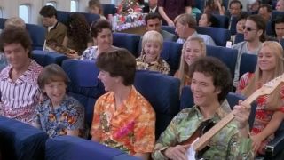 The whole Brady Bunch together sitting on a plane with Greg holding a guitar in A Very Brady Sequel