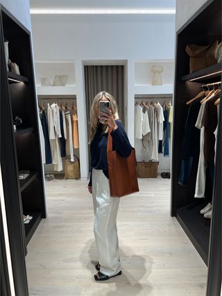 Eliza Huber in the dressing room at Banana Republic wearing a navy blue cashmere sweater with white linen pants and a brown leather bag.