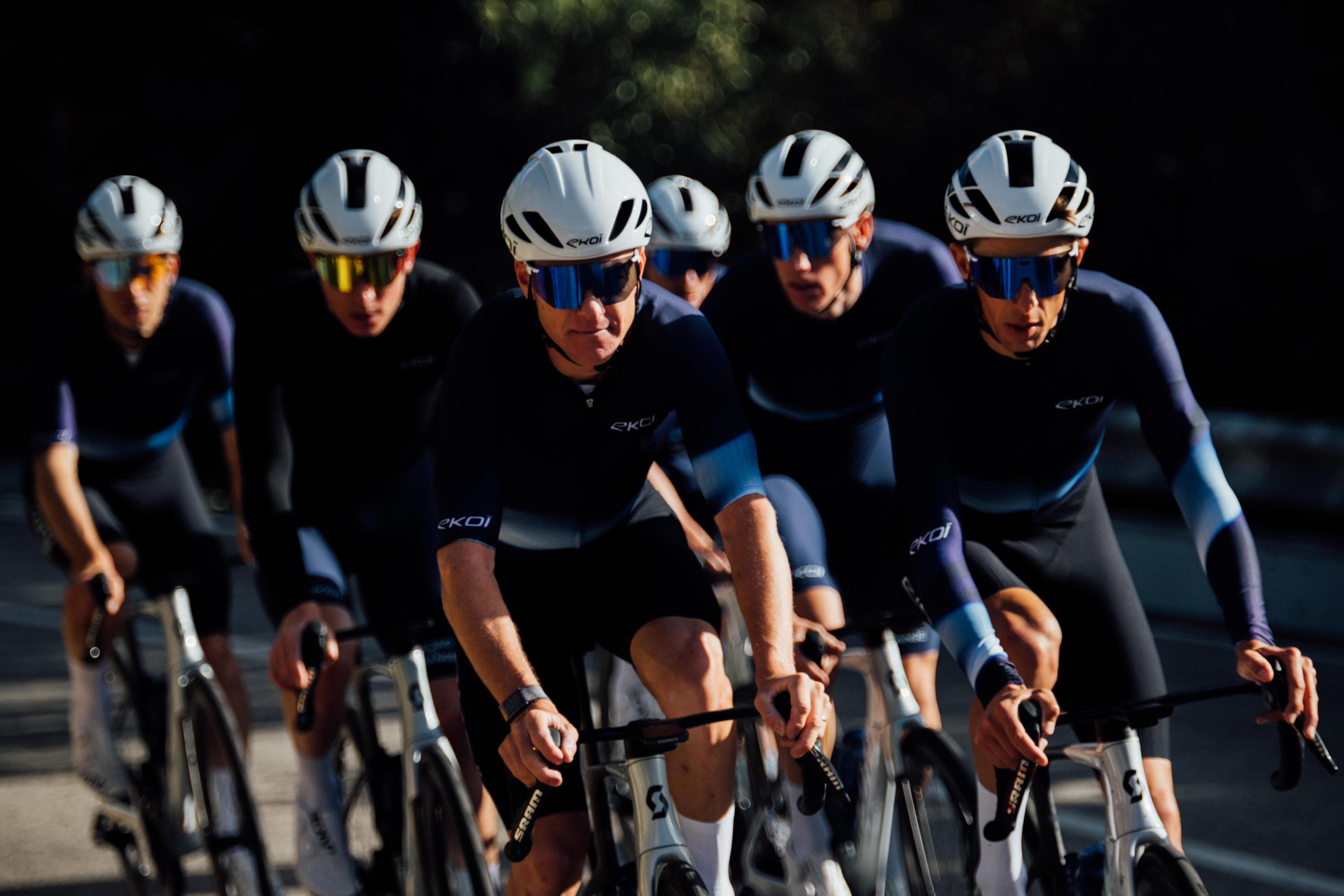 Six cyclists with light helmets and dark clothing riding toward the camera