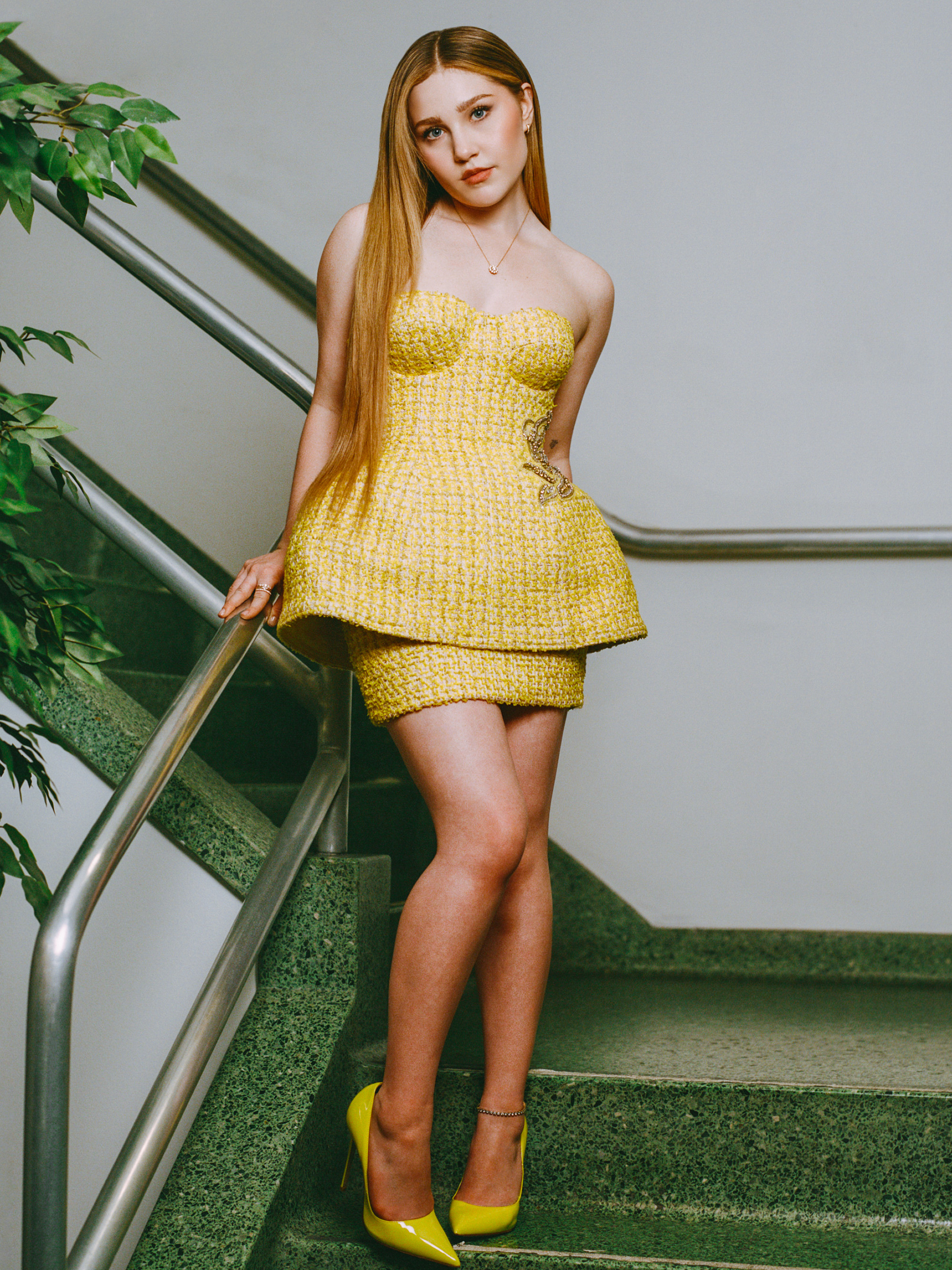 Portrait of actress Ella Anderson for her interview with Who What Wear. She is wearing a yellow tweed set consisting of a strapless bustier top with peplum detail and a pencil skirt and neon yellow pumps.
