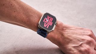 The Apple Watch Ultra 2 on a man's wrist, showing a watch face of red Roman numerals on a black background.