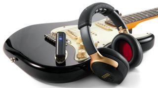 A photo showing the Positive Grid Spark NEO headphones and dongle with a black Stratocaster or Stratocaster-style guitar
