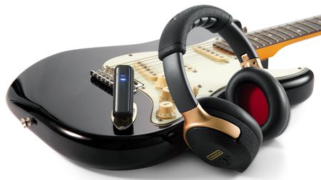 A photo showing the Positive Grid Spark NEO headphones and dongle with a black Stratocaster or Stratocaster-style guitar