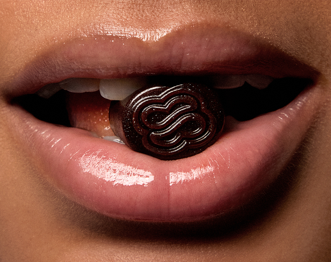 Woman holding one of Sakara's Metabolism Bite gummy supplements between her teeth.