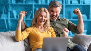 Couple sitting on sofa with a laptop and looking excited.