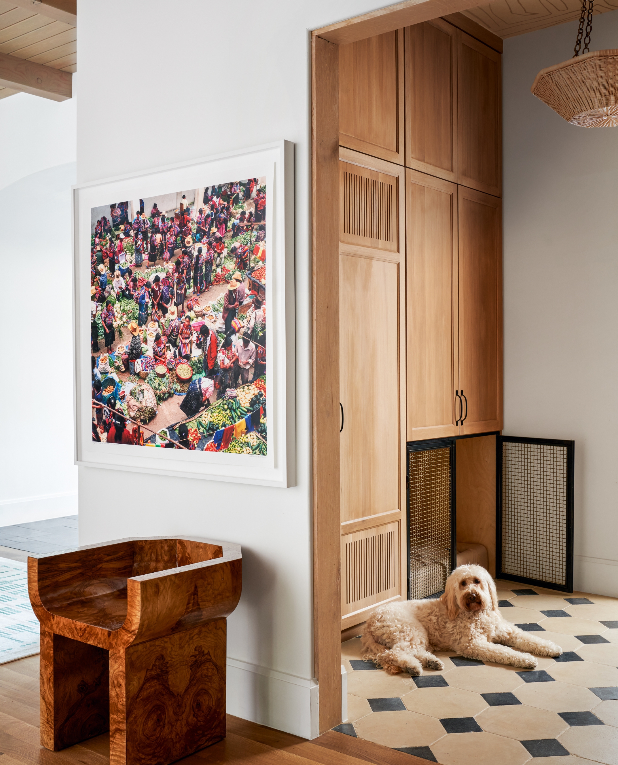 A white walled corridor with a view into the boot room, which has tall, wooden cupboards and a built in dog crate.