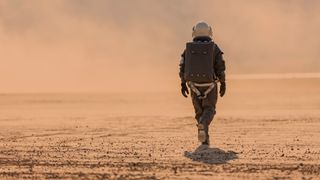 a person in a brown spacesuit walking on a reddish-orange desert
