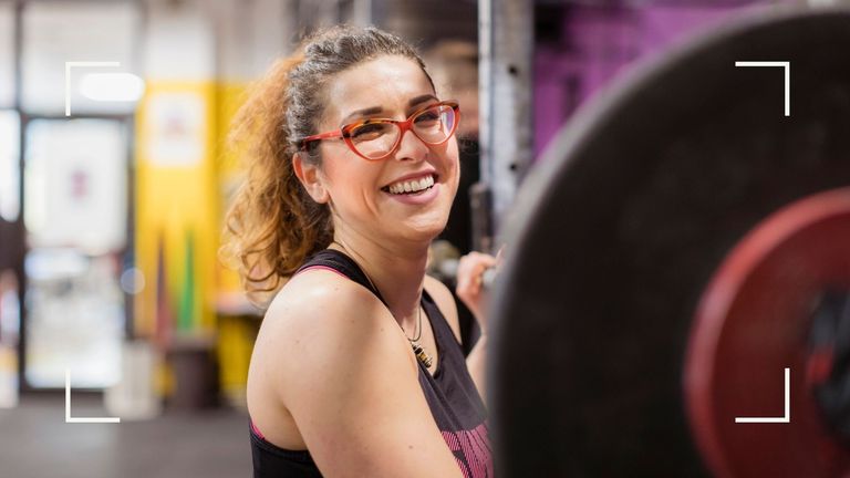 Woman wearing glasses lining up to a barbell about to work out after finding out how much exercise per week she needs to do