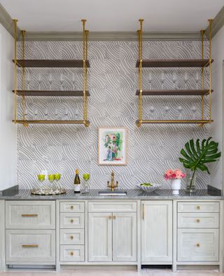 bar with gray green cabinets and tiles above with brass taps on small sink