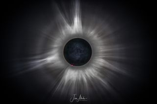 the eclipse looks like an eye, with a dark center and radiating white rings with corona details and small pink filament eruptions visible.