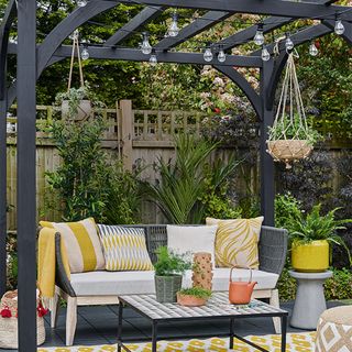 grey painted pergola with lights and potted plant on table