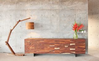 Concrete wall with large wooden dresser and standard lamp