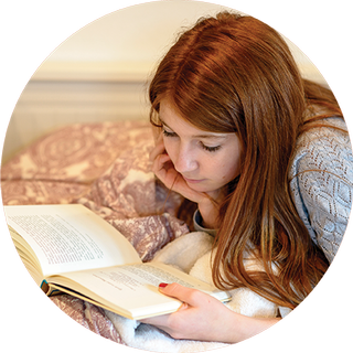 Image of young girl lying on the bed reading a book