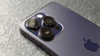 En mörkgrå iPhone 14 Pro Max ligger med baksidan vänd uppåt på ett grått bord.