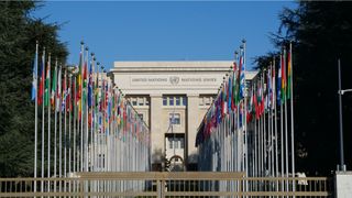 A view of the United Nations building with each nation flag lined up outside beneath a blue sky