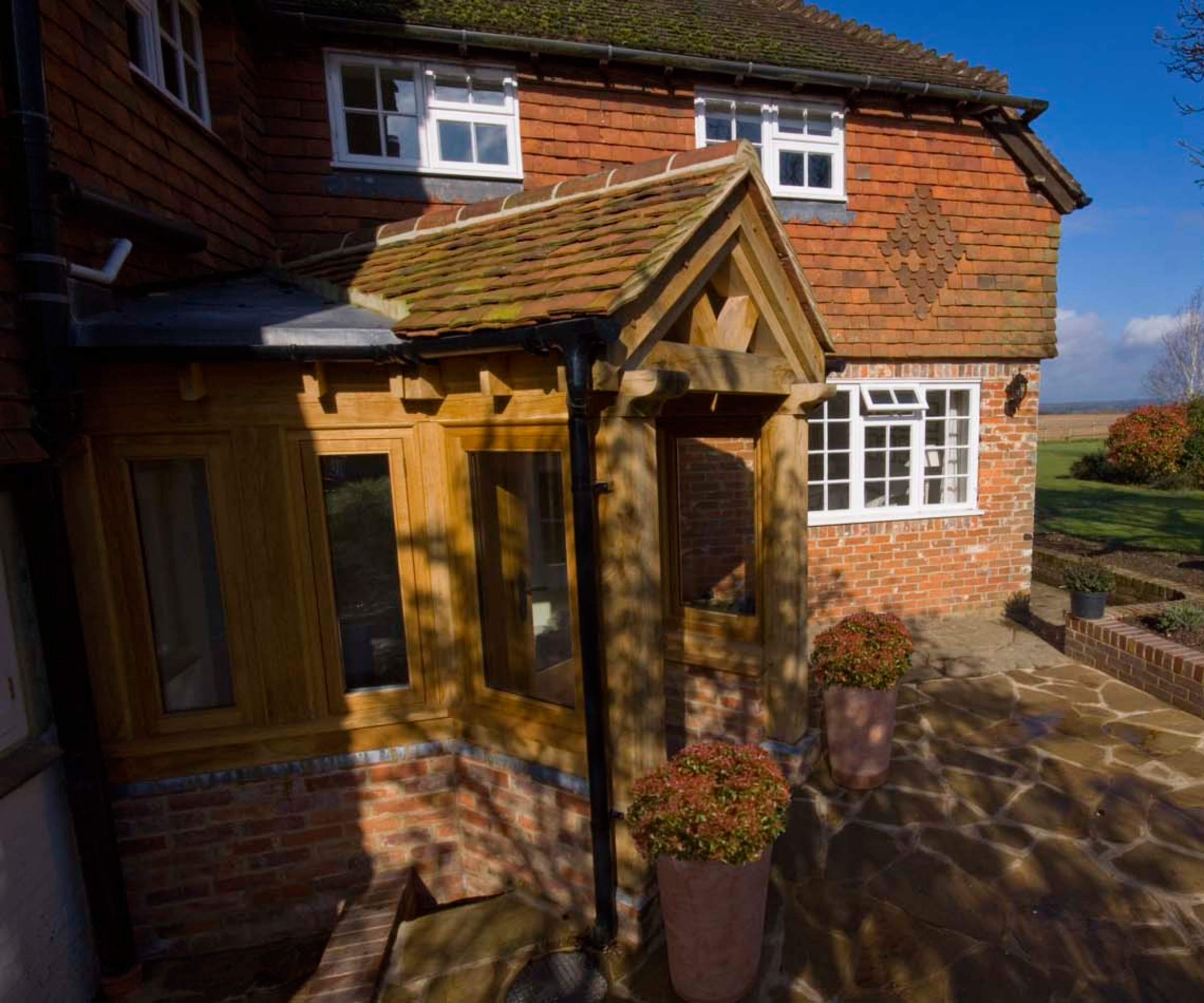 fully enclosed oak frame porch with windows and low dwarf brick wall on brick and tile clad house