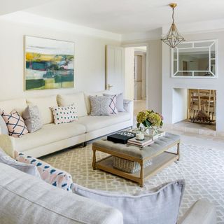 White living room with white couches, fire place, wooden padded coffee table and beige patterned rug