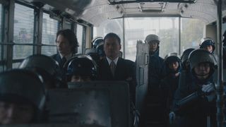 Ansel Elgort and Ken Watanabe sitting on a bus with armored police officers in Tokyo Vice