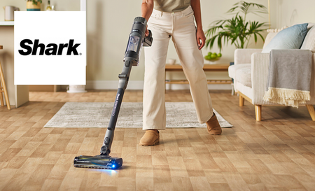 Shark logo top left with a picture of a woman hoovering the living room