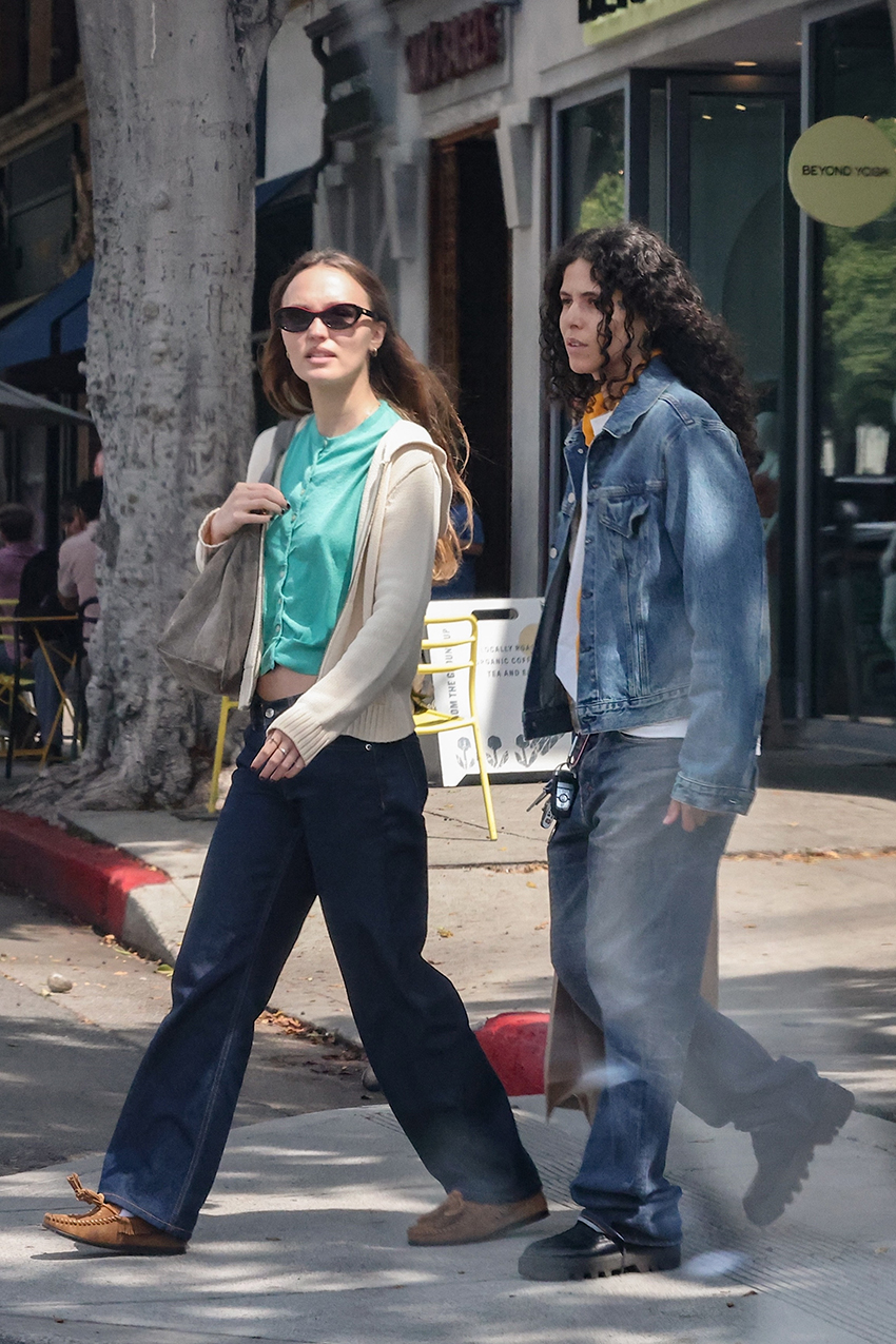 Lily Rose Depp wearing a teal shirt, beige hoodie, indigo jeans, suede shoulder bag, and tan suede loafers