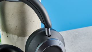 the soundcore space one pro headphones; a photograph of a pair of black over-ear headphones with cushioned cups and a closeup of the soft headband, photographed in front of a blue background