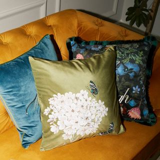 A trio of cushions with floral butterfly designs arranged on a yellow sofa