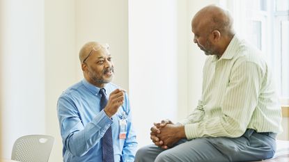 An older man in a doctor's office listens to his doctor as he explains something.