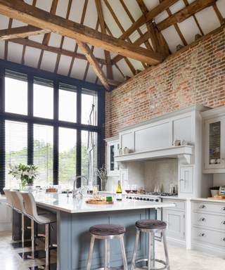 Modern kitchen ideas merging old with new, with modern cabinetry and white worktops in a tall room with exposed brick wall and beamed ceiling.