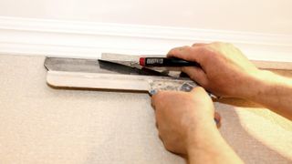 Hands cutting top of wallpaper with a blade