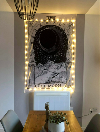 A white wall with a grey section painted, along with a tarot card style tapestry and some fairy lights.