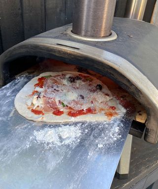 sliding a pizza into an outdoor pizza oven