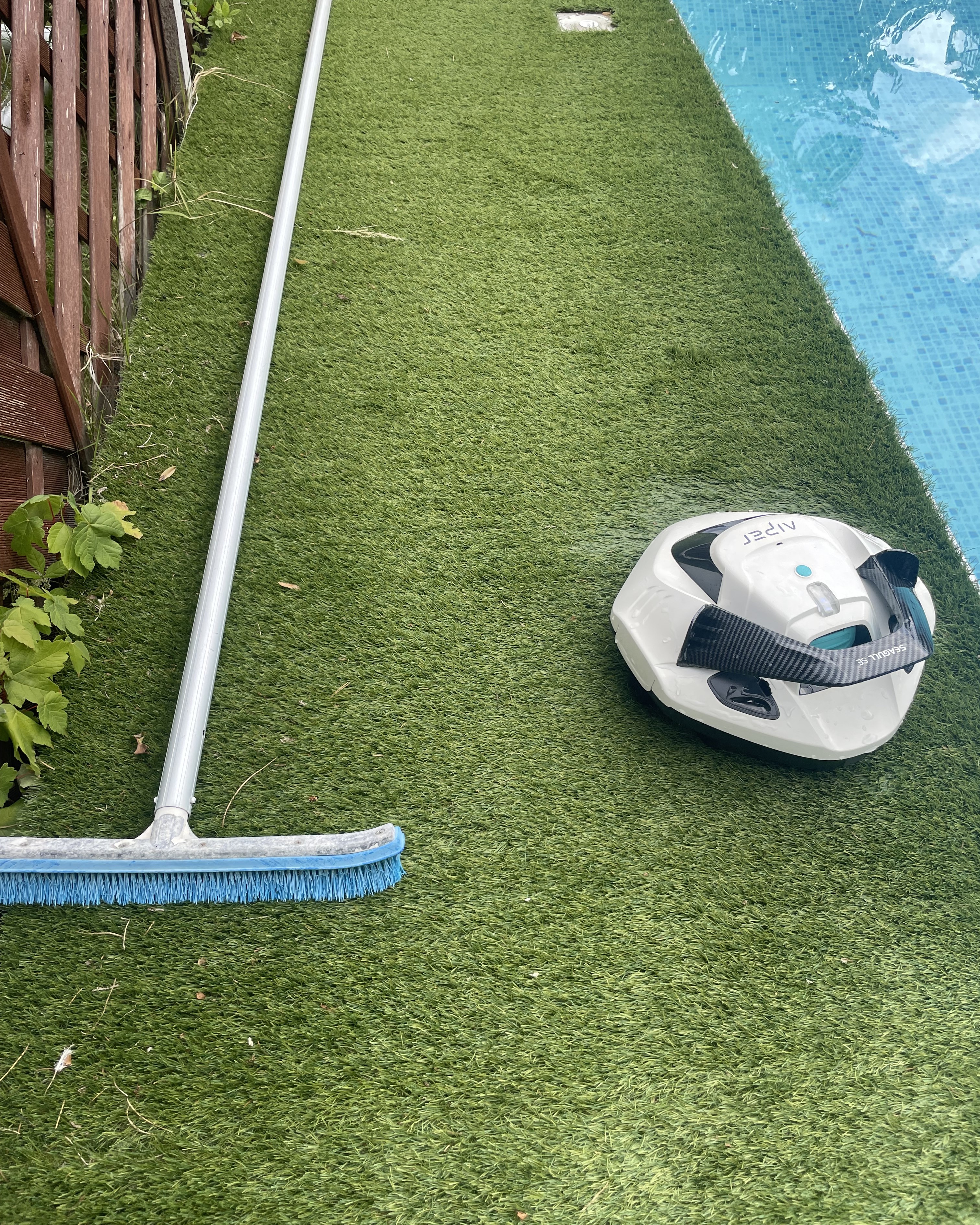A pool cleaner on astroturf next to a pool