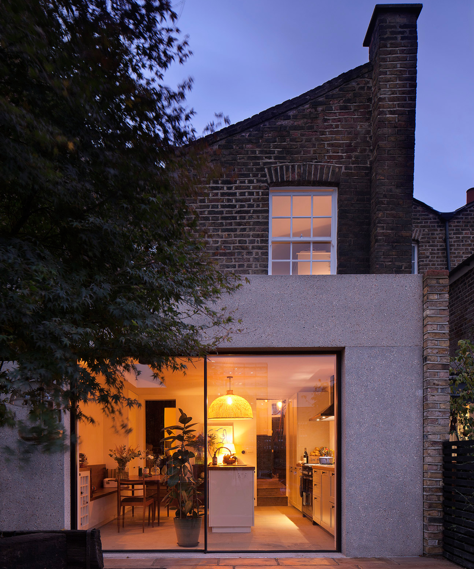 single storey rear extension with concrete exterior and large slimline sliding doors showing kitchen area lit up inside