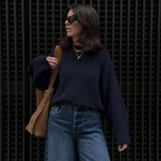 Woman wears navy cashmere jumper, blue jeans, brown suede bag