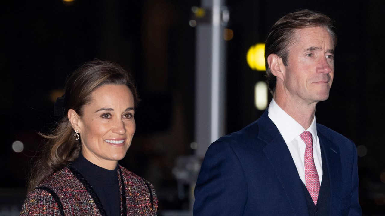 Pippa Middleton wears a black top with a mottled red jacket and her husband James Matthews wears a navy suit, white shirt, and red tie