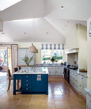 An example of kitchen extension ideas showing a blue kitchen island with a marble worktop in front of a range cooker and white kitchen cabinets